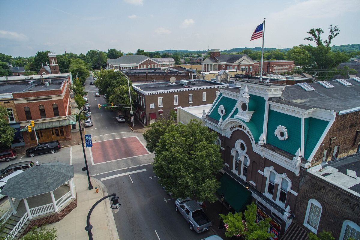 Aerial view of downtown Cleveland, with the teal-and-white Victorian front of a historic hall, a gazebo, and a tree-lined street under a flag