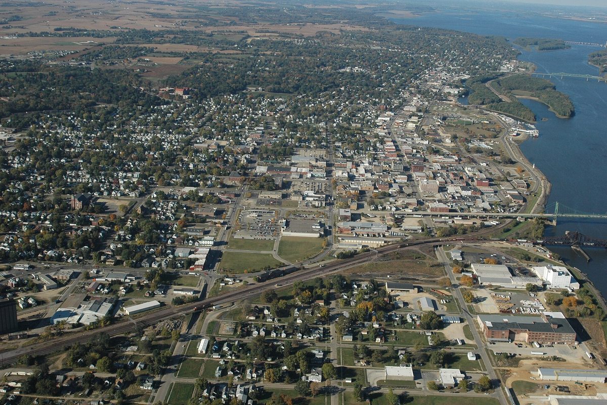 Aerial view of Clinton spreading back from a wide river, with a railroad line across the foreground and bridges over the water on the right