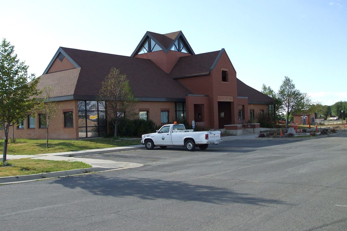Clinton City Hall, a brick building with a steep brown roof and a peaked skylight, with a white city pickup truck parked in the lot