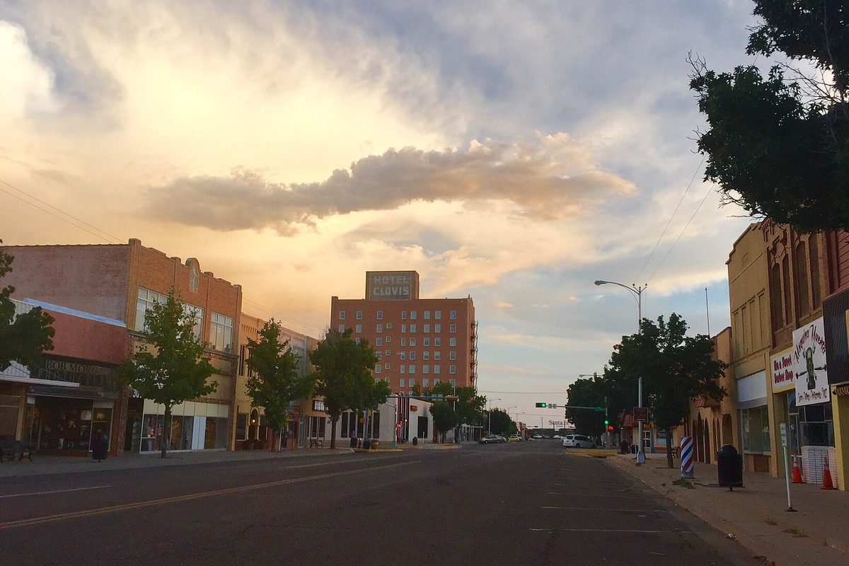 Looking south on Main Street in downtown Clovis at sunset, with brick storefronts and the tall Hotel Clovis building under a golden sky