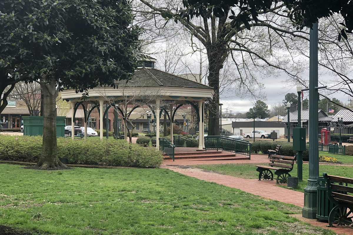 The white gazebo on Collierville's town square, with brick paths, green benches, lawn and bare trees on a gray day
