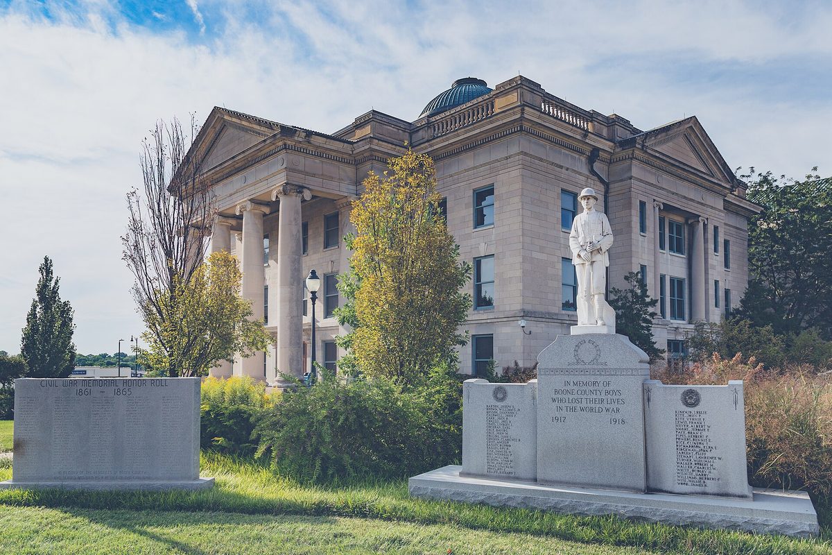 The columned limestone Boone County Courthouse in Columbia under a blue sky, with a World War I memorial statue of a soldier on the lawn in front