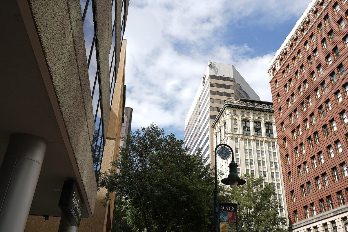 Downtown Columbia seen from the sidewalk, with a white office tower, an ornate older high-rise and a red brick building behind trees and a black street lamp