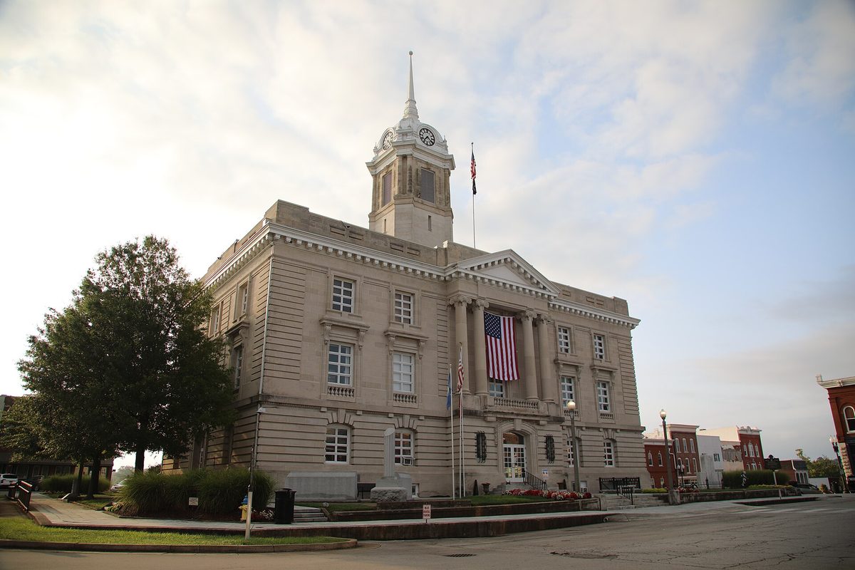 The pale stone Maury County Courthouse in downtown Columbia, with a clock tower, columns and a large American flag hung over the entrance