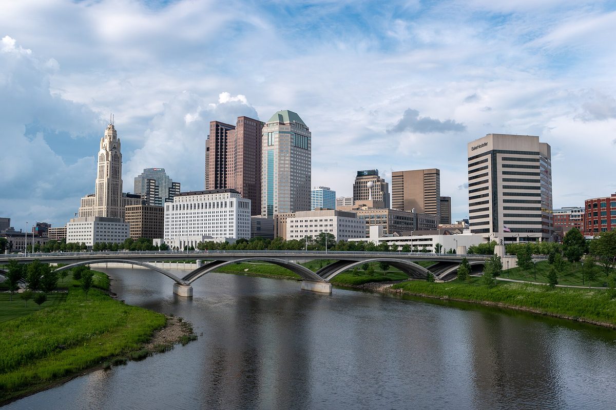 Downtown Columbus skyline with the LeVeque Tower on the left, seen across the Scioto River and a low arched bridge from the Main Street Bridge