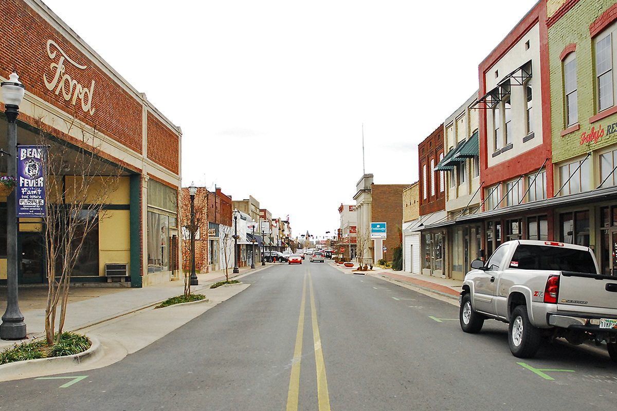 A street in Conway's historic downtown lined with brick storefronts, an old Ford sign on the corner building and a pickup parked at the curb