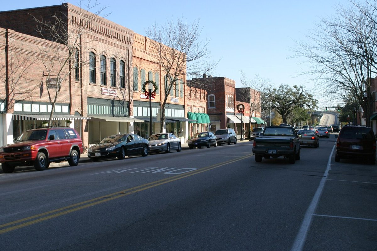 Brick storefronts with green awnings along Main Street in downtown Conway, cars parked at the curb and a holiday wreath on a lamp post