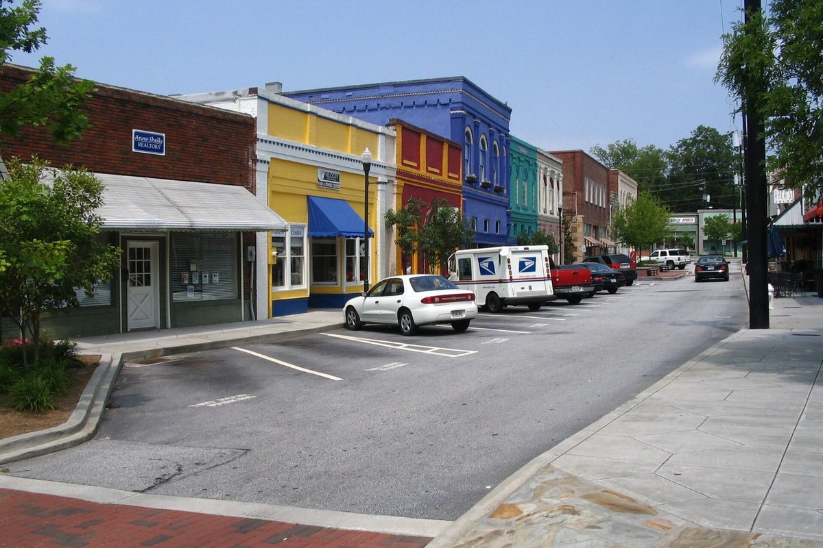 A row of brightly painted storefronts in yellow, blue, red and teal in Olde Town Conyers, with a mail truck and parked cars along the street