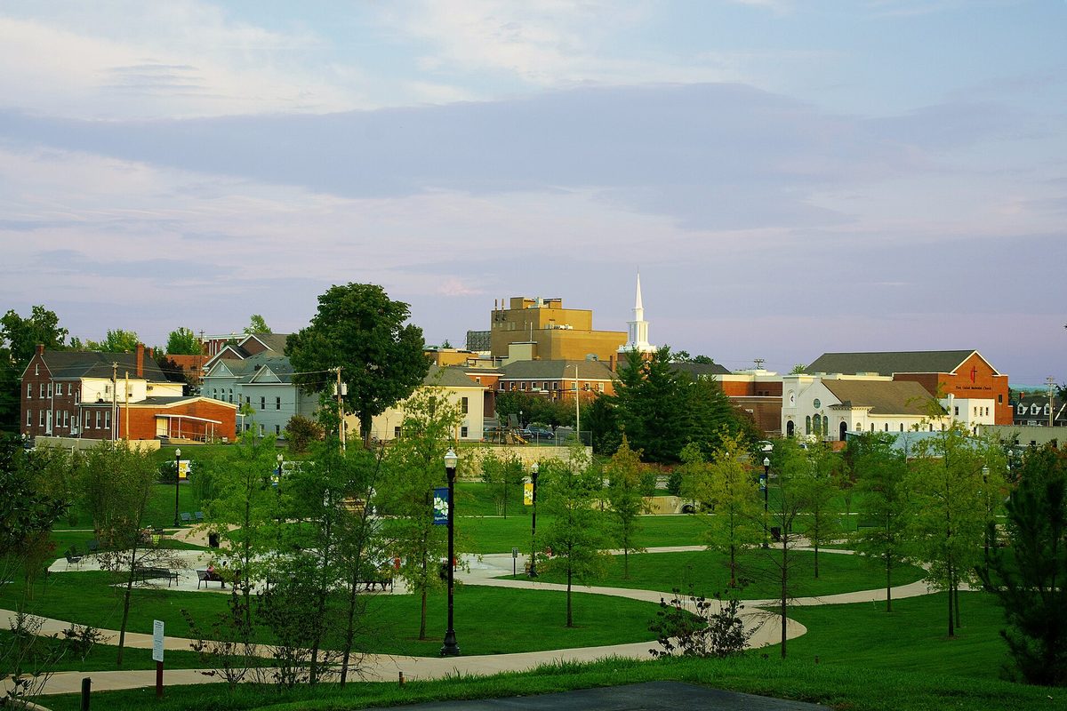 Cookeville at sunset looking east, with the curving paths and lamp posts of Dogwood Park in front of brick buildings and a white church steeple