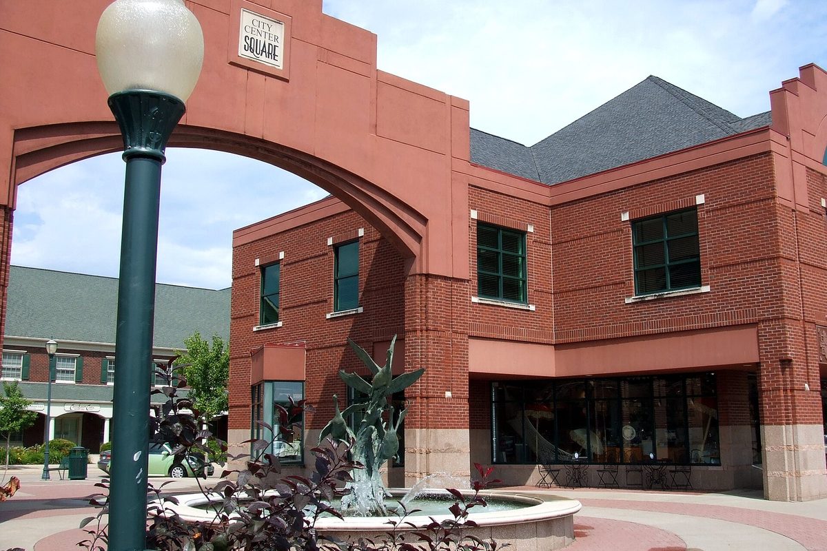 A red brick arch marked City Center Square over a plaza with a fountain and flowers in downtown Coralville