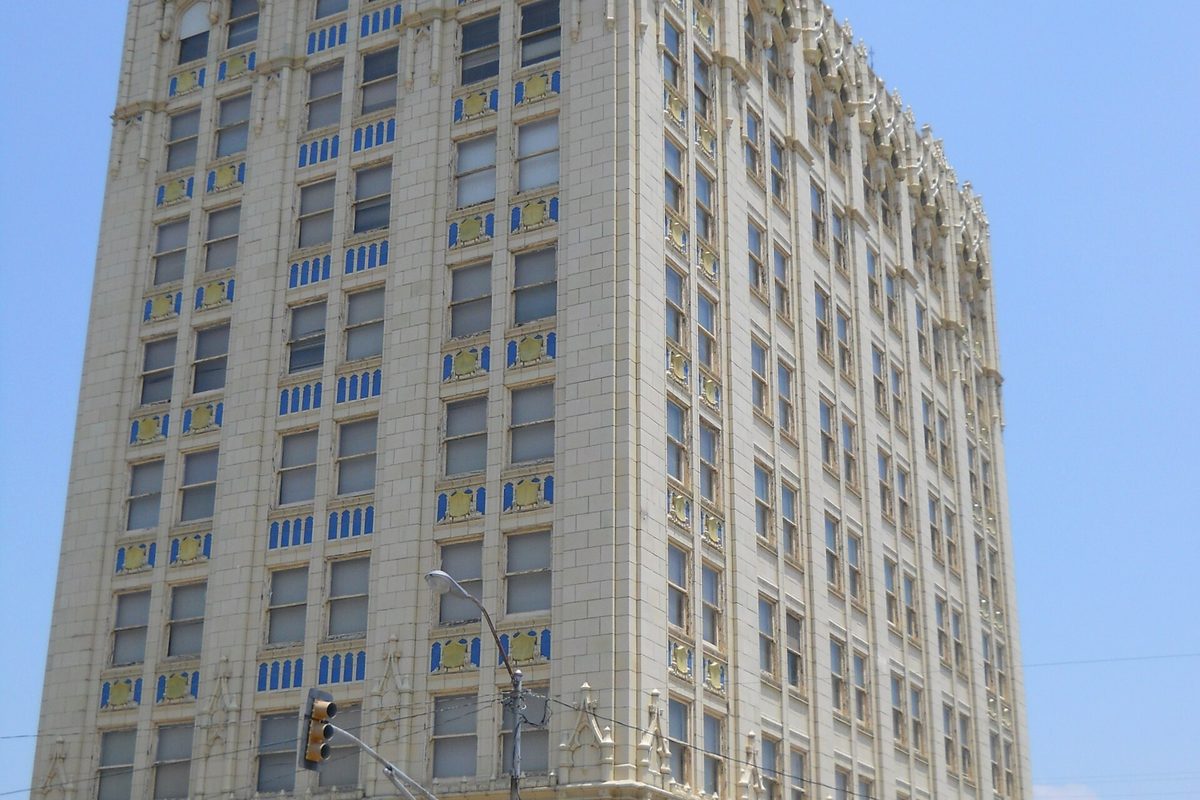 The State National Bank Building in downtown Corsicana, a tall cream terra-cotta tower with blue and gold panels under its windows, a traffic light in front