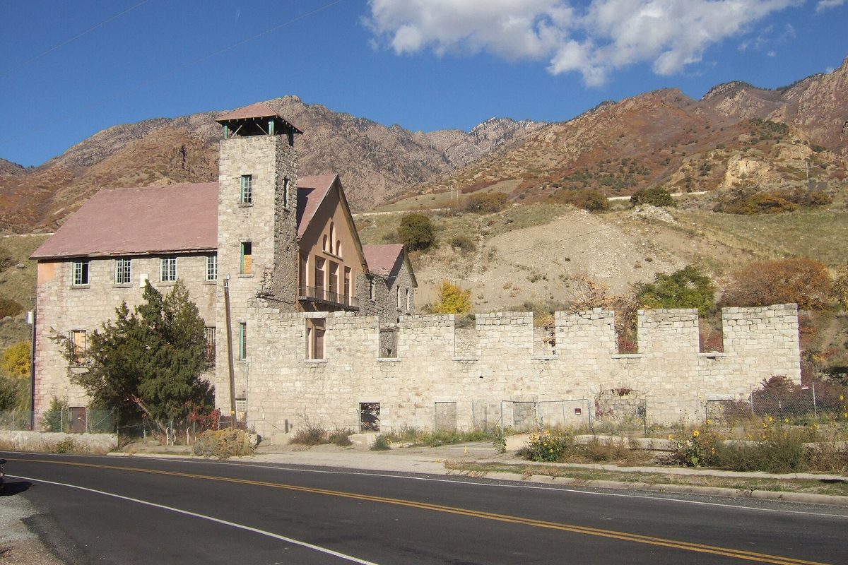 The stone ruin of the Cottonwood Paper Mill, with a square tower and a crenellated wall, beside a road at the foot of rocky mountains