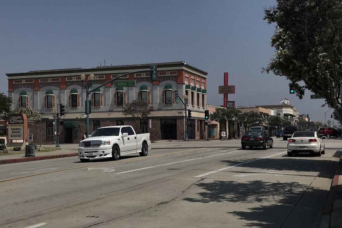 A two-story red brick building with arched windows on a downtown Covina corner, with a white pickup and two cars passing on the street