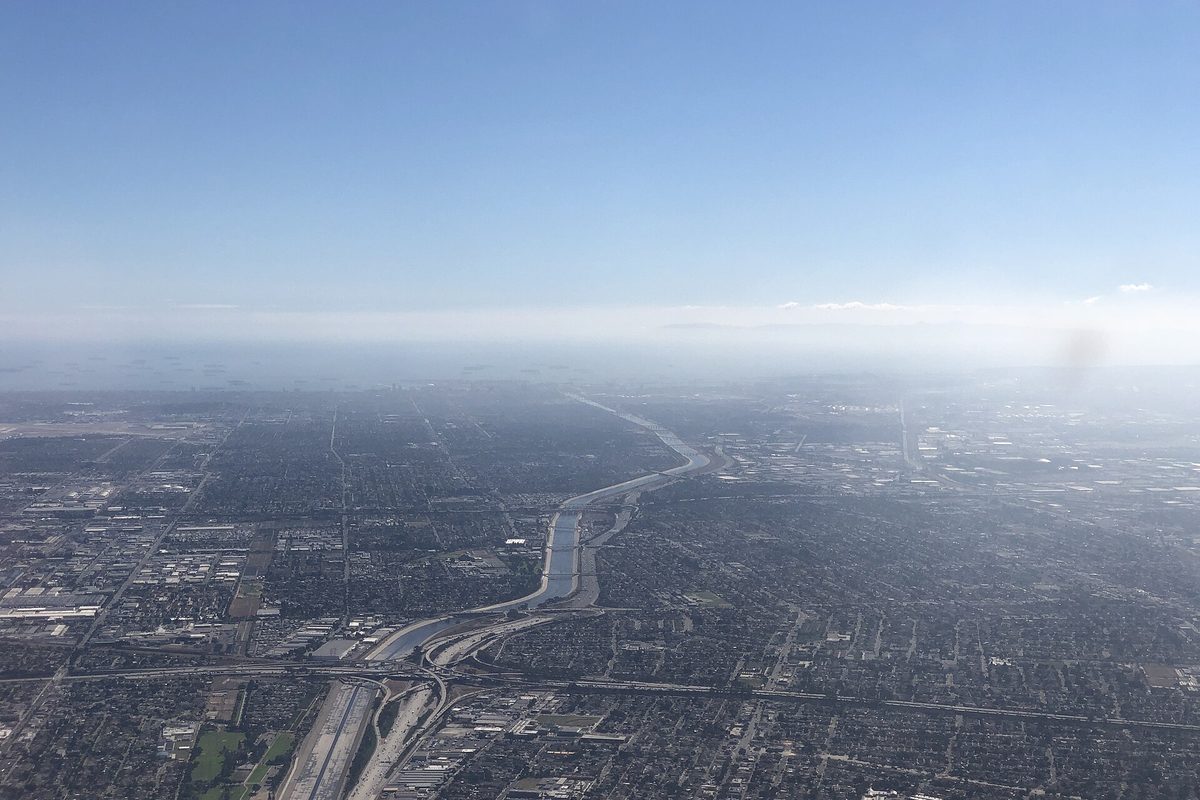 Aerial view looking southwest along the concrete Los Angeles River channel and Interstate 710 over the dense grid of homes in southern Los Angeles County, under a hazy sky