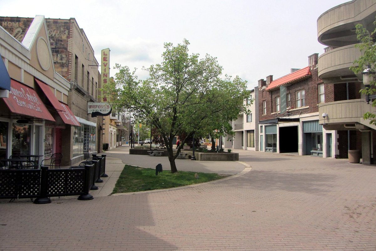 A brick-paved pedestrian street in downtown Cuyahoga Falls, lined with low brick storefronts, red awnings and a young tree in a grass bed