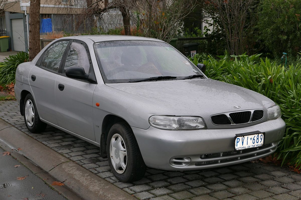 A silver Daewoo Nubira sedan parked on wet brick pavers in front of a green hedge