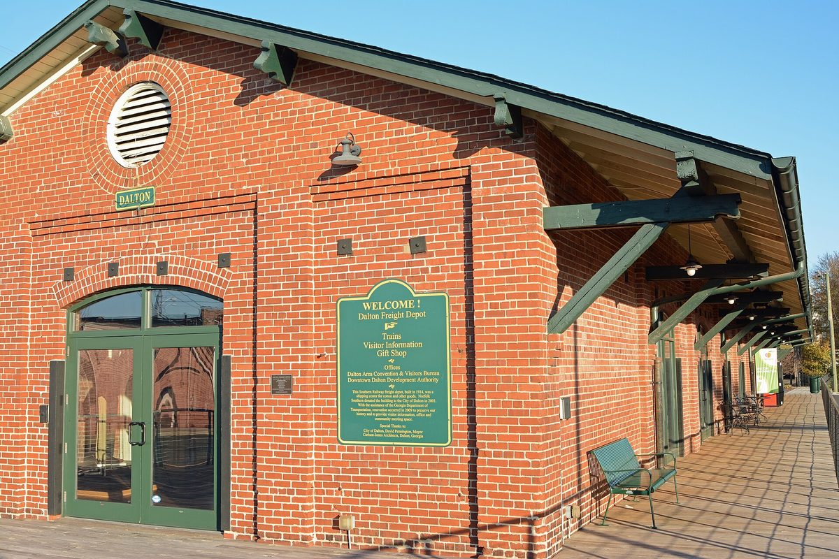 The red brick Dalton Freight Depot with green doors, a round vent and a green welcome sign listing the visitor center and gift shop