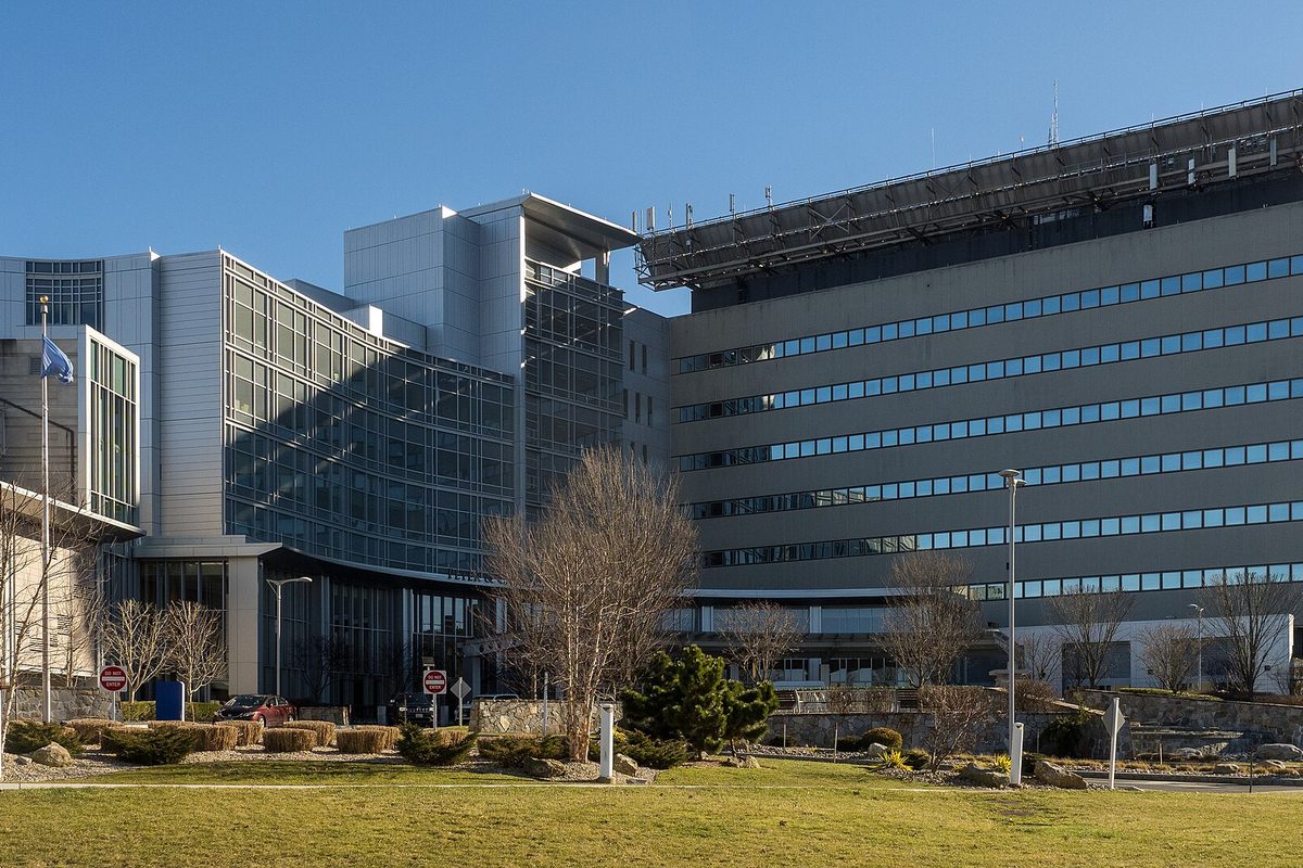 Danbury Hospital's large glass and concrete building with a flagpole, young bare trees and a lawn in front, under a clear blue sky