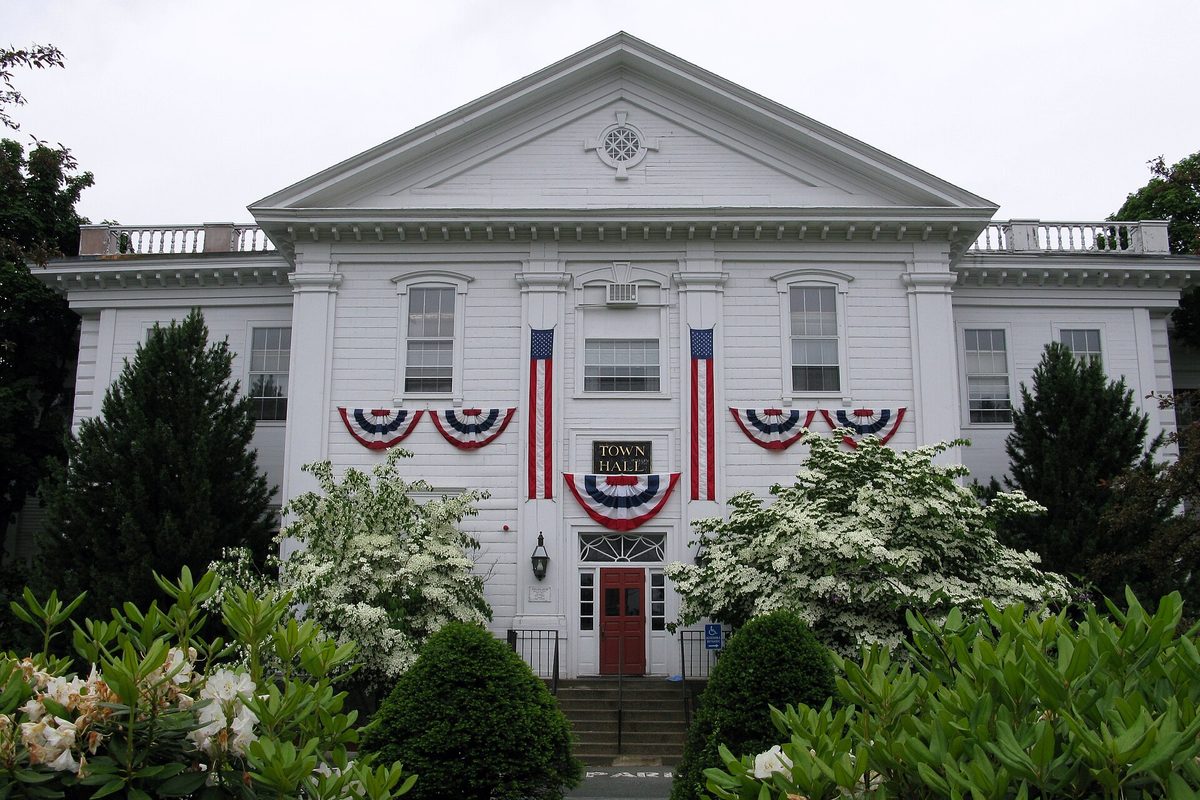 Danvers Town Hall, a white Greek Revival building hung with red, white and blue bunting, behind flowering dogwoods and shrubs