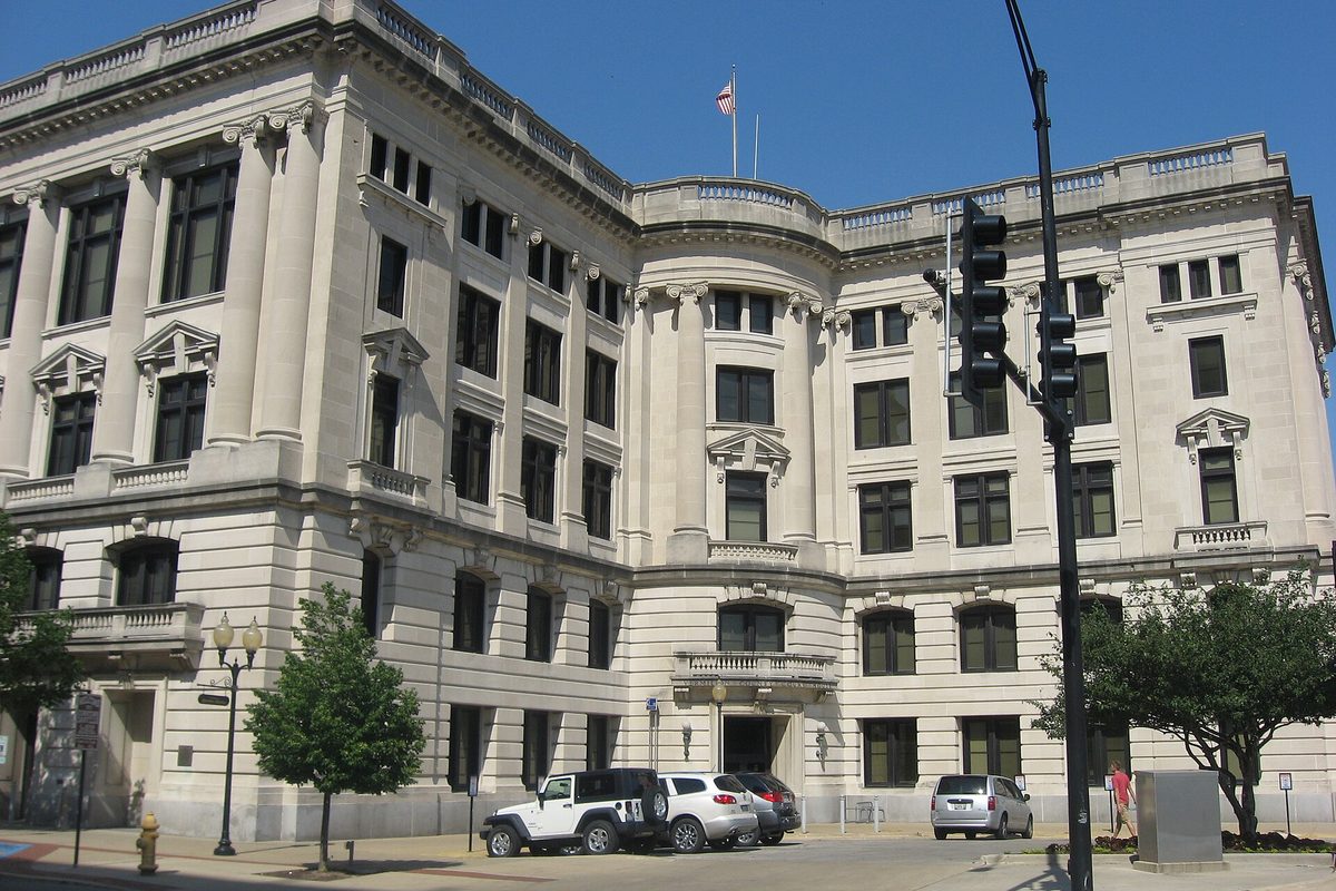 The white stone Vermilion County Courthouse in downtown Danville, with cars parked out front and a traffic signal at the corner
