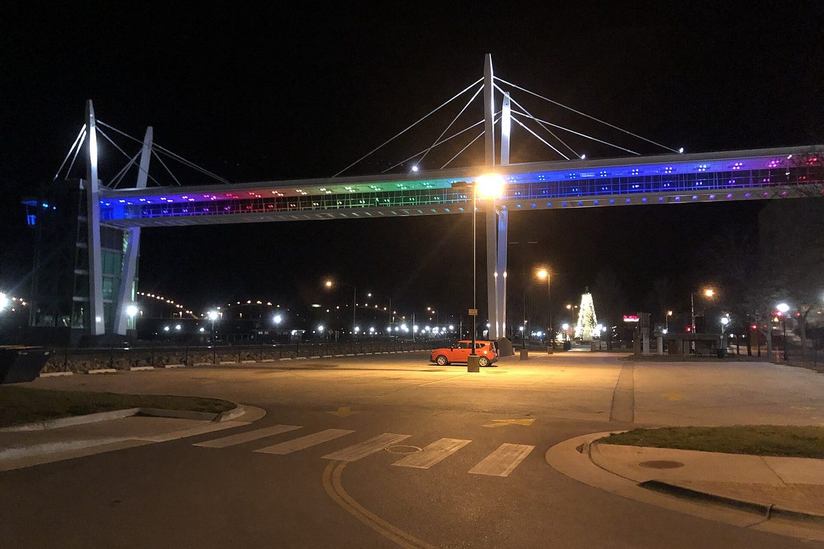 Davenport's cable-stayed sky bridge lit in bands of color at night, with an orange car parked under a bright streetlight below it
