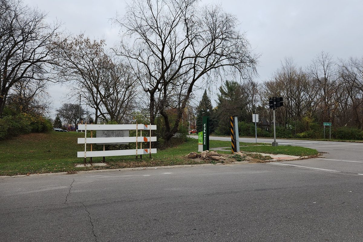 White barrier gates beside the road at Hines Drive and Outer Drive in Dearborn Heights, with bare trees under a gray sky