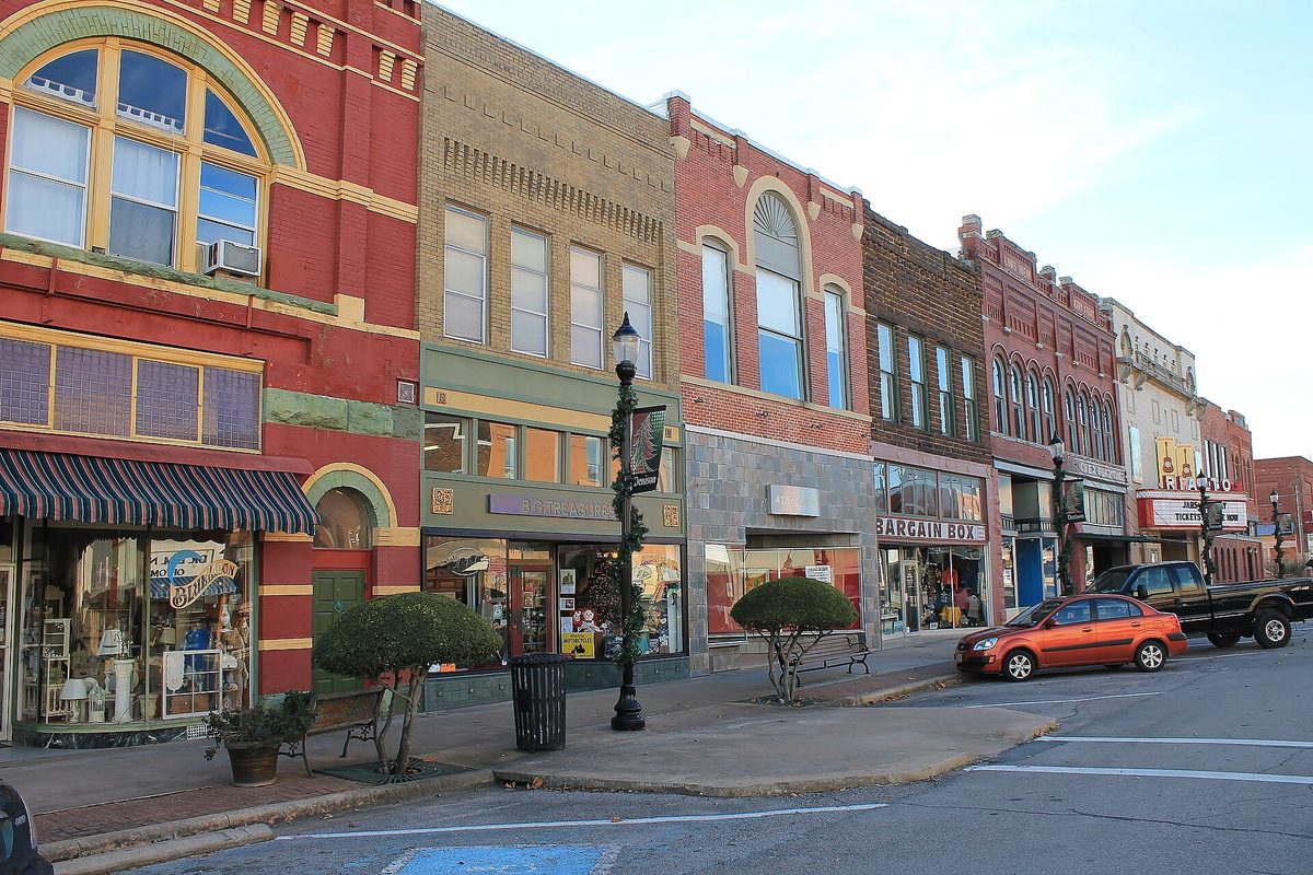 Red and tan brick storefronts with arched upper windows along Main Street in Denison's commercial historic district, with green lamp posts and an orange car parked at the curb