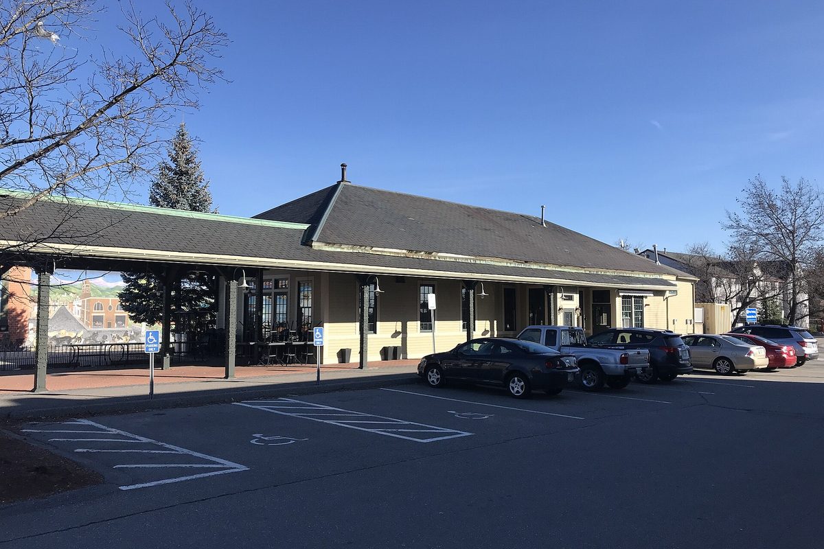 The old Derry Station depot, a long low building with a gray roof and a wide canopy over the platform, cars parked in the lot in front