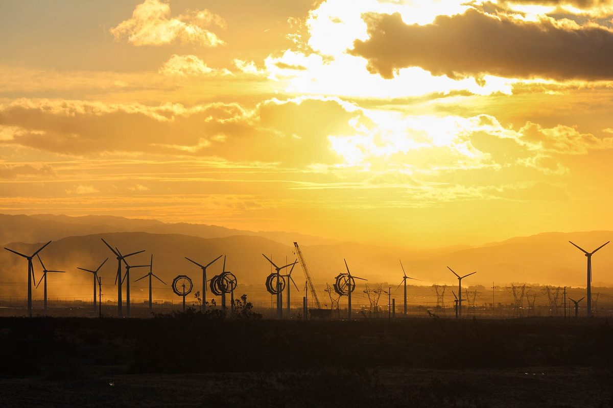 Wind turbines silhouetted against a golden sunrise sky over hills along Highway 62 near Desert Hot Springs