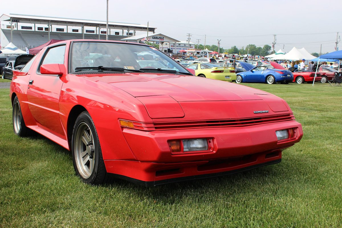 A red Conquest hatchback coupe with wide fenders parked on the grass at a car show