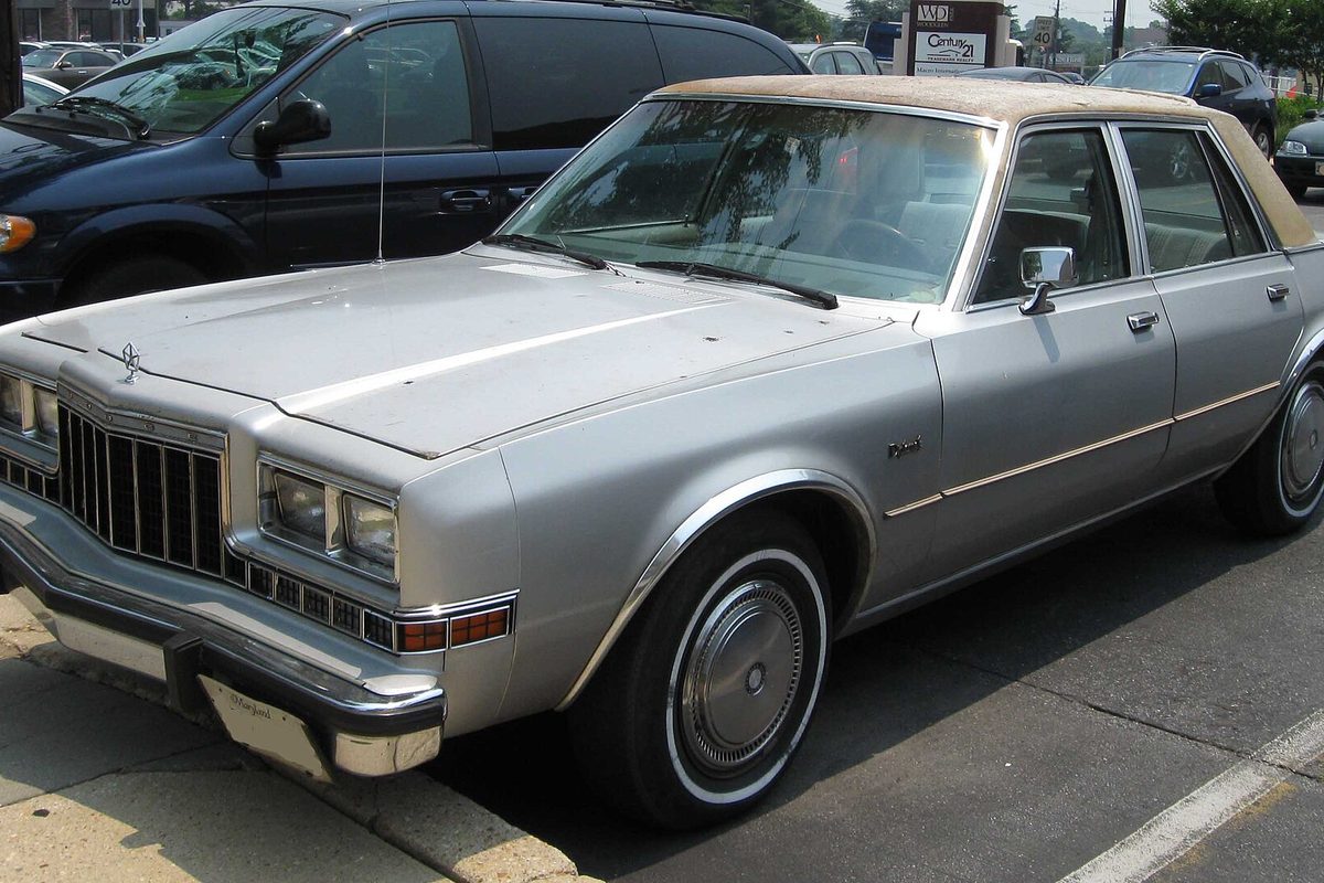 A silver Dodge Diplomat four-door sedan with a tan vinyl roof and whitewall tires parked at a curb