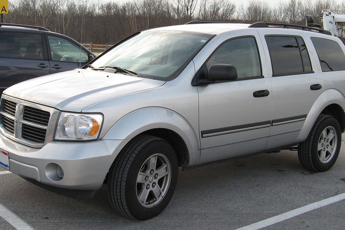 A silver second-generation Dodge Durango SUV with roof rails, parked in a lot with bare winter trees behind it