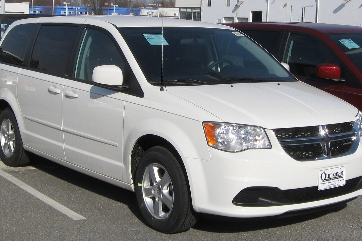 A white 2011 Dodge Grand Caravan minivan with silver alloy wheels on a dealer lot, a sticker on the windshield