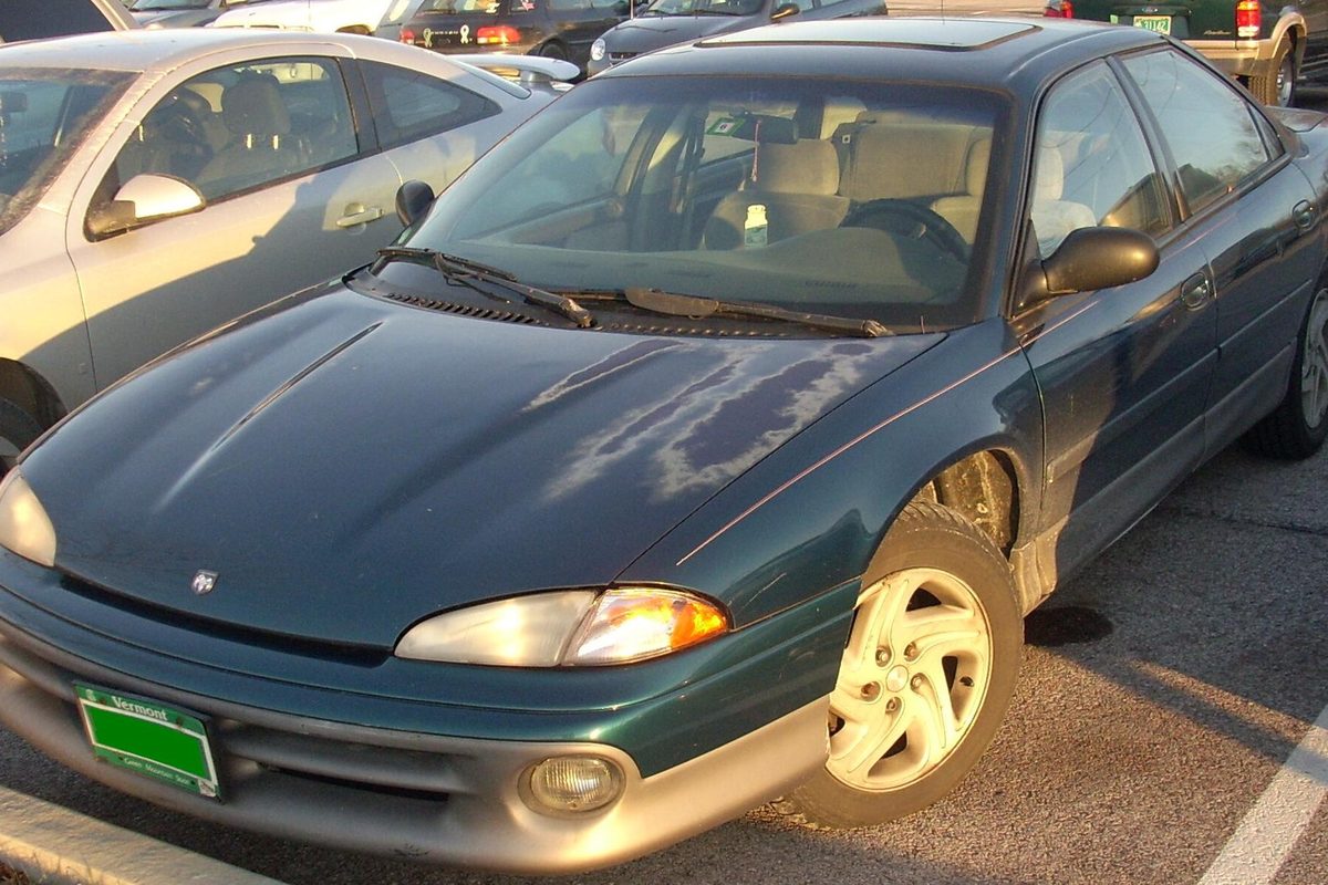 A dark green first-generation Dodge Intrepid sedan with sun-faded paint peeling on the hood, parked in a lot