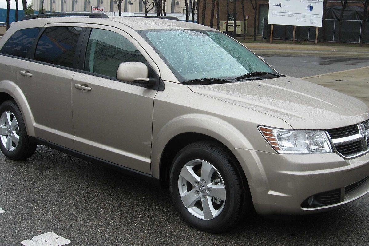 A champagne-colored 2009 Dodge Journey crossover parked on a wet city street, rain beaded on its windshield
