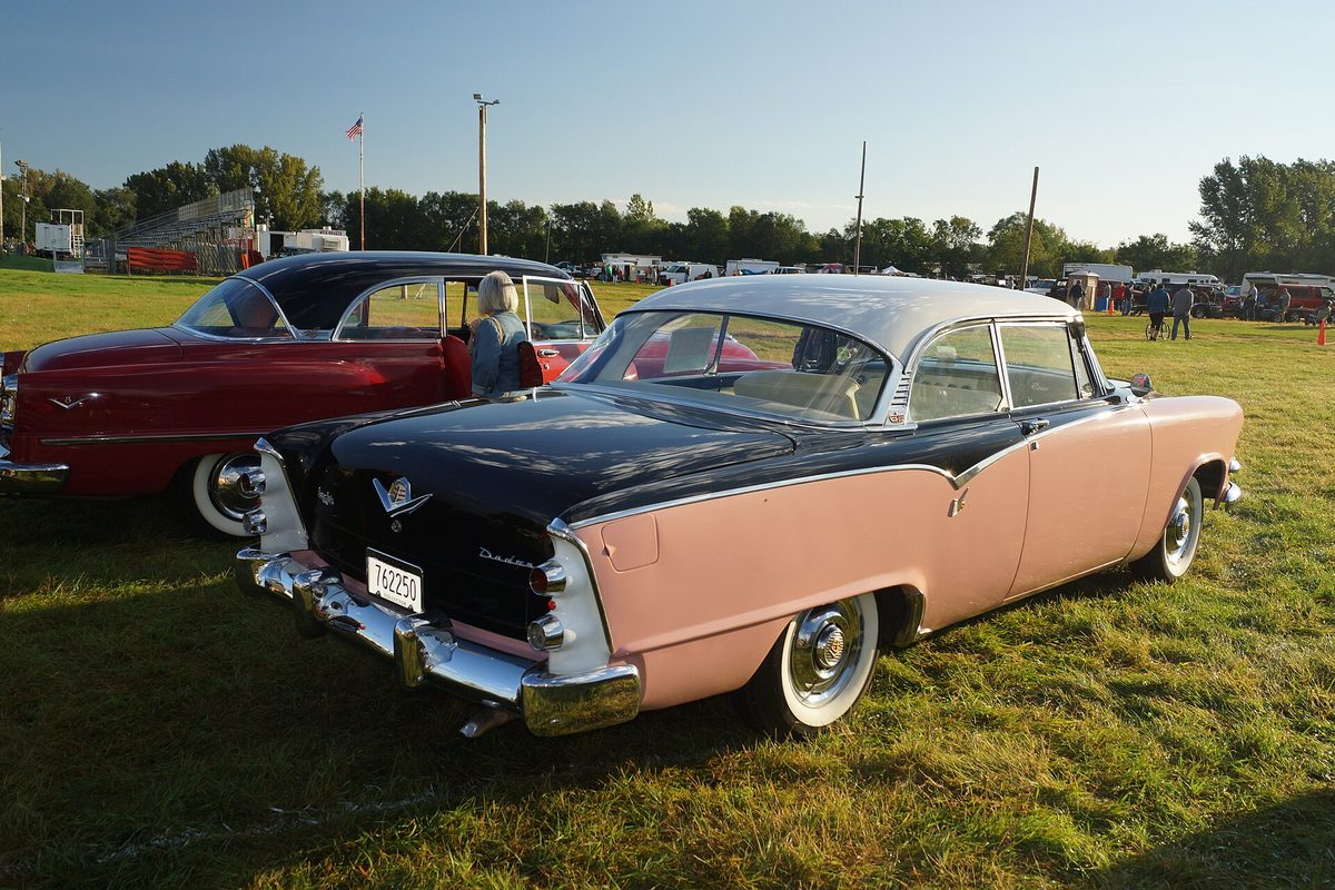 Rear view of a pink and black two-tone 1955 Dodge Coronet Lancer hardtop with whitewall tires at an outdoor car show