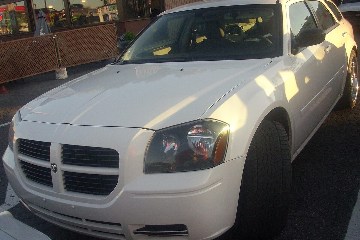 A white Dodge Magnum wagon, front three-quarter view, parked outside a restaurant in low evening sun