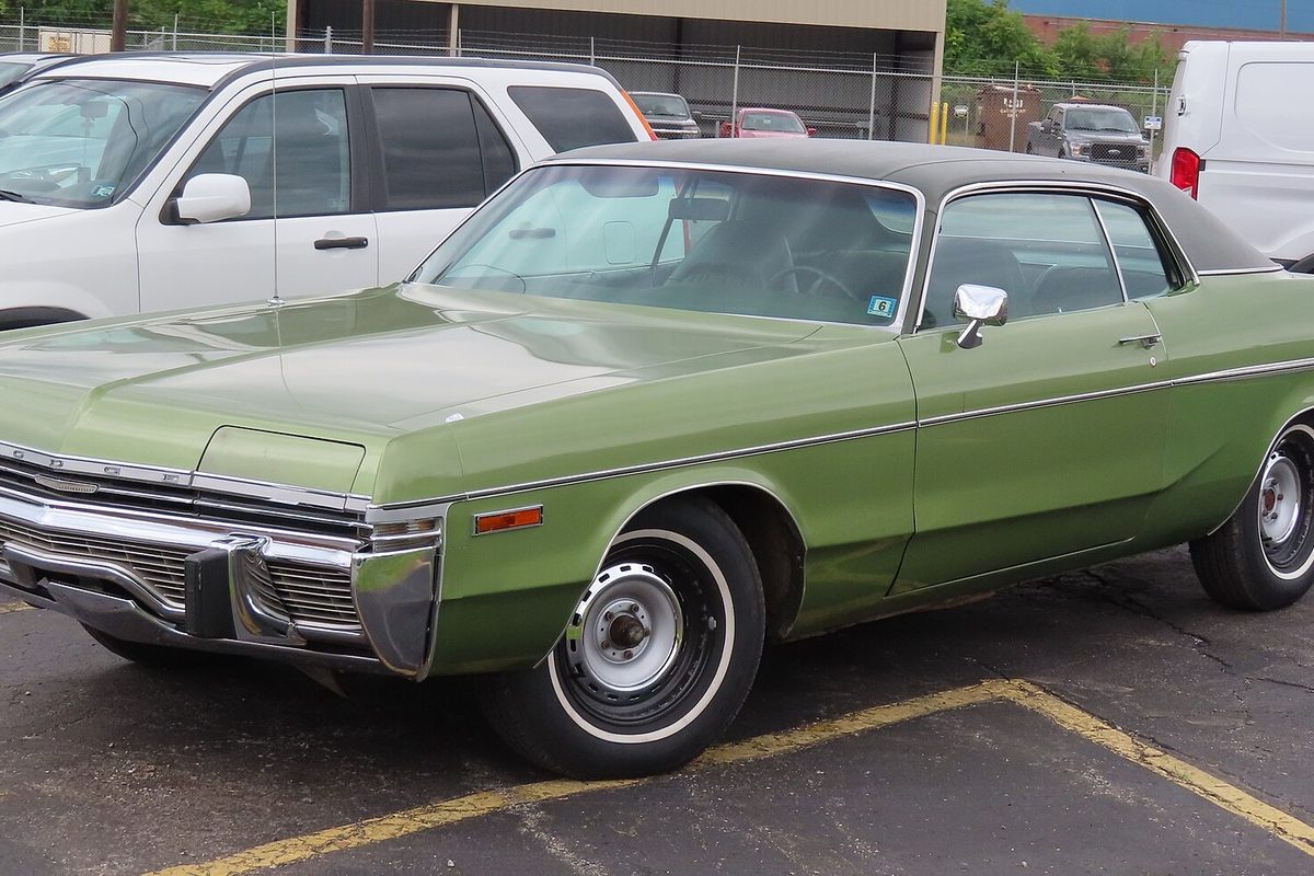 A light green metallic 1973 Dodge Monaco two-door hardtop with a dark vinyl roof and whitewall tires, parked in a lot