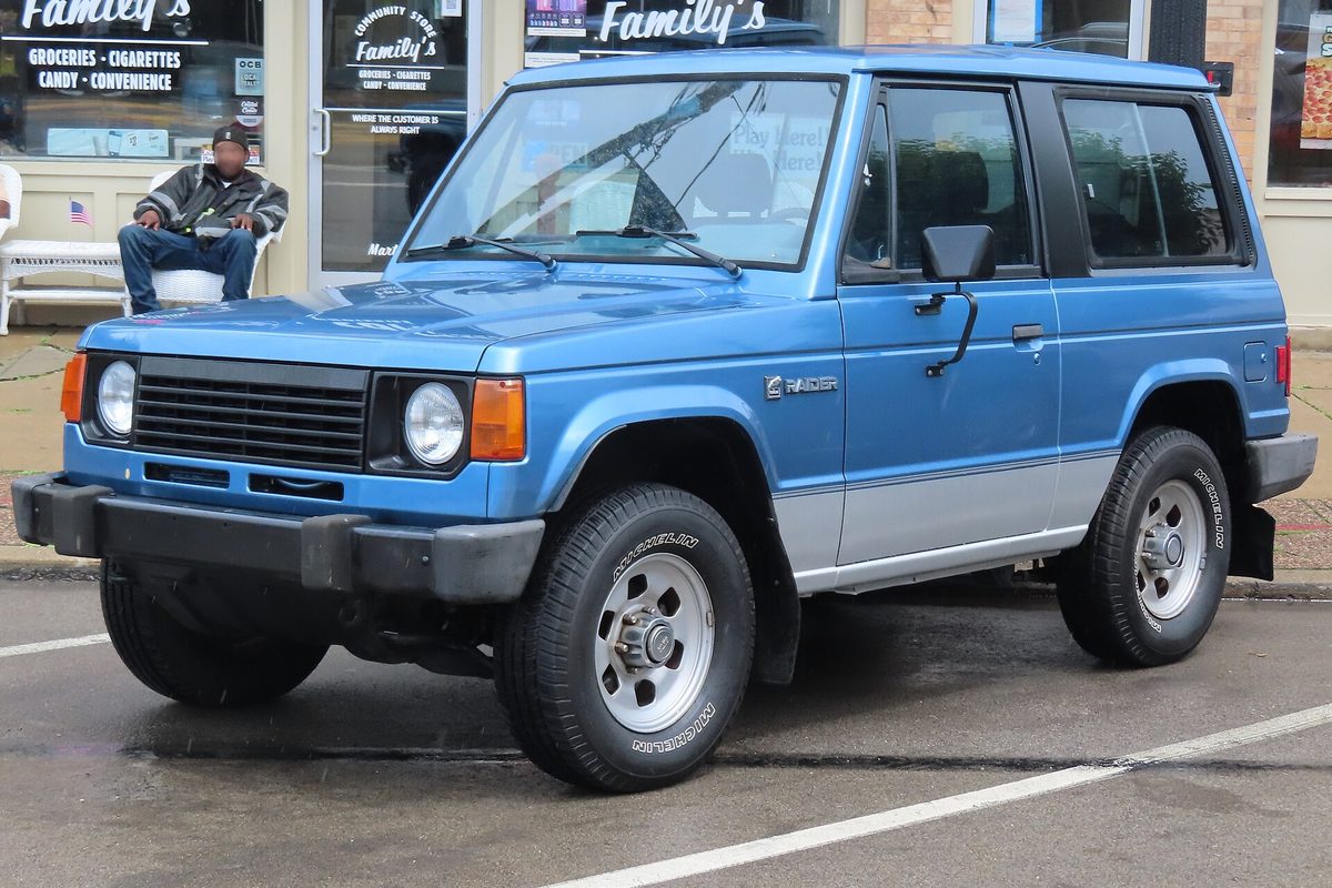 A two-tone blue and silver two-door Dodge Raider SUV parked on a wet street outside a corner store