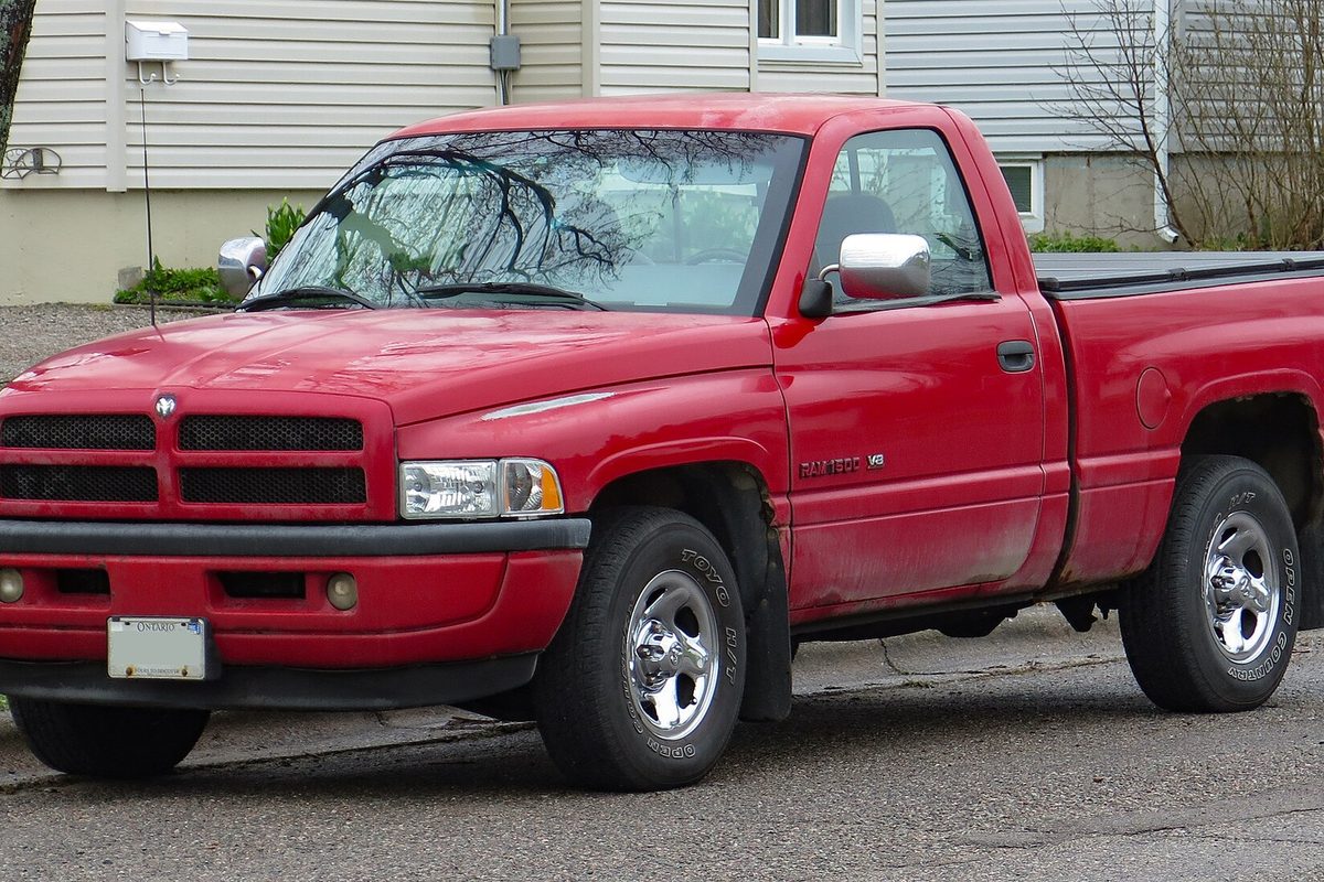 A red 1996 Dodge Ram 1500 regular-cab short-bed pickup with chrome wheels, parked on a street in front of a house