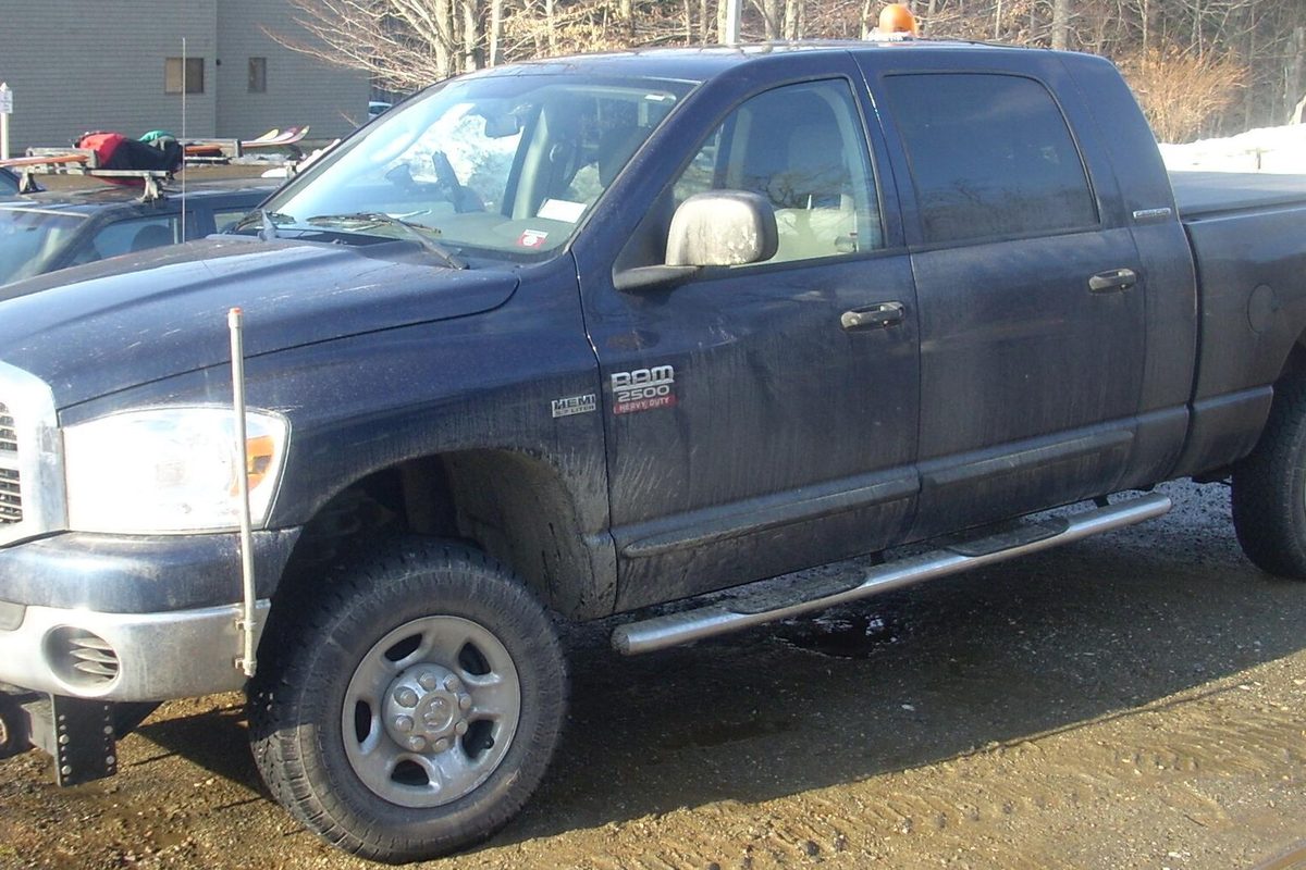 A mud-splashed dark blue Dodge Ram 2500 four-door pickup with chrome running boards, parked on a dirt lot