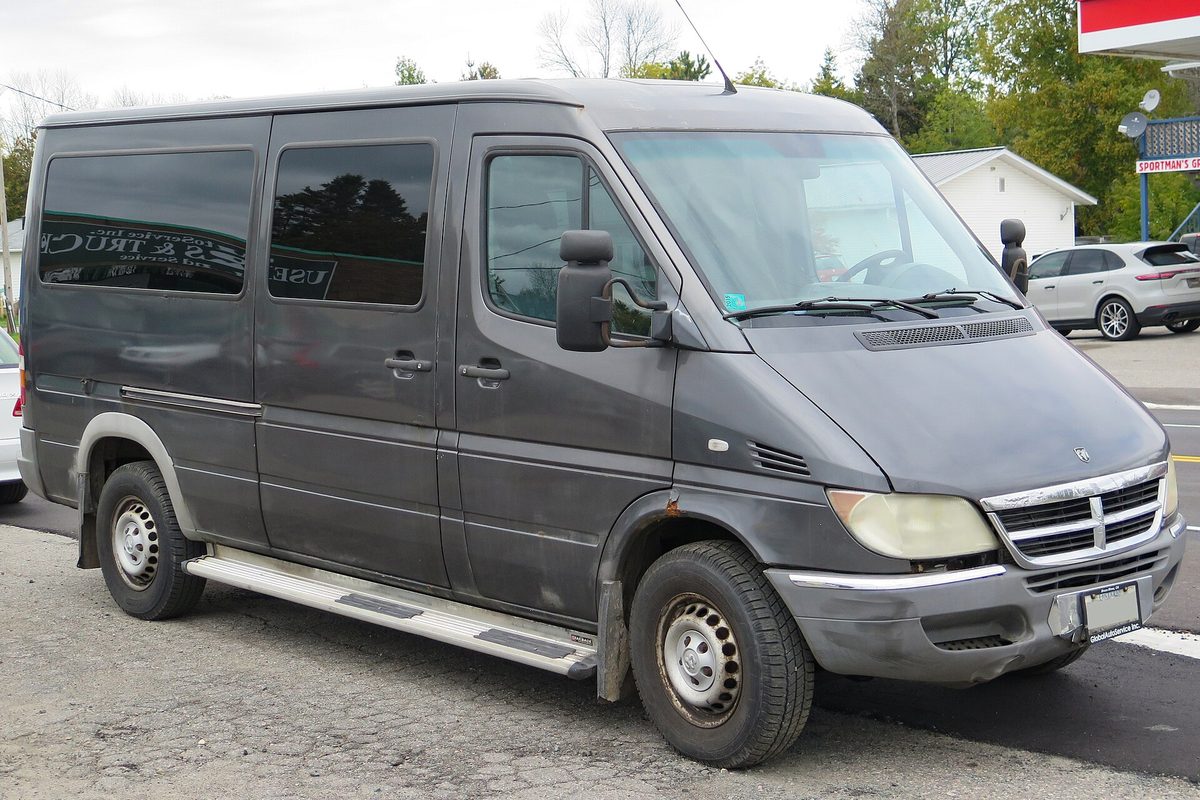 A dark gray first-generation Dodge Sprinter passenger van with tinted windows and side steps, parked on a gravel lot