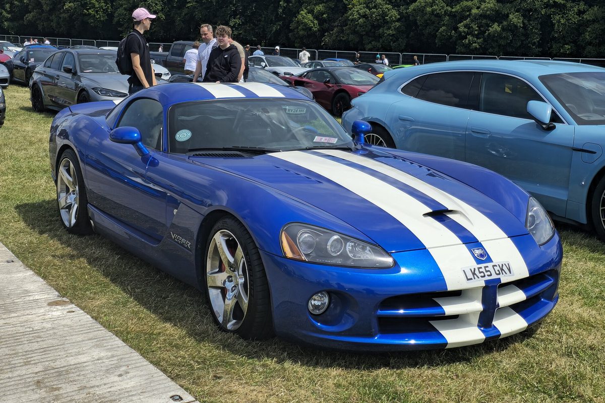 A blue Dodge Viper SRT-10 coupe with twin white stripes, parked on grass at an outdoor car show