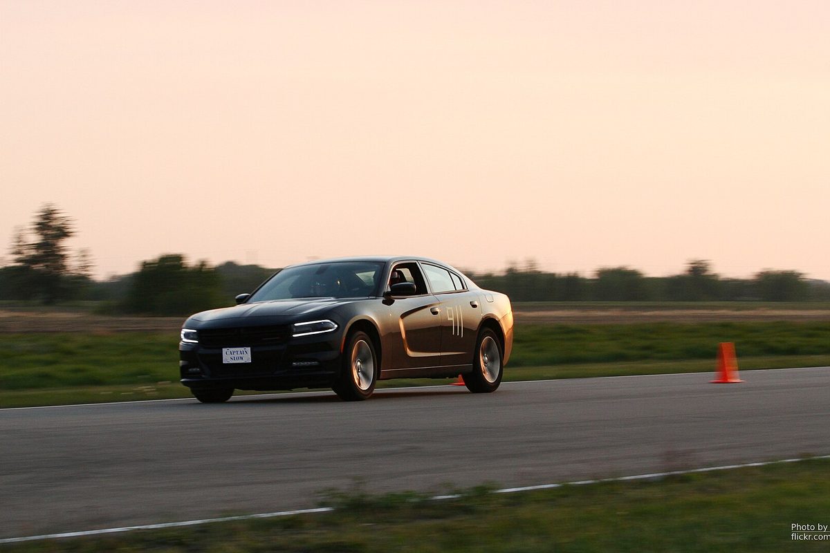 A dark gray Dodge Charger sedan running an autocross course at dusk, with an orange traffic cone beside the track