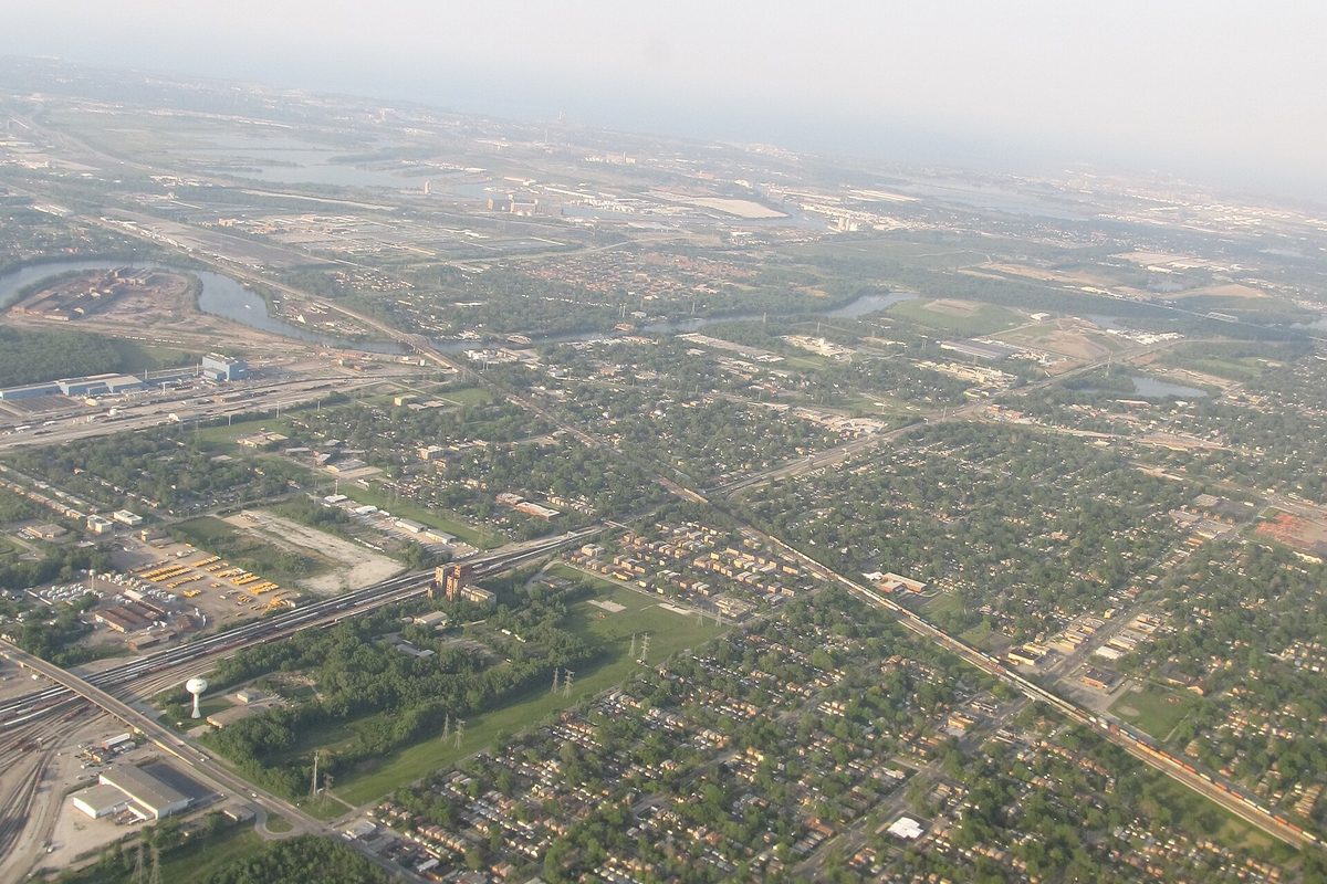 Aerial view of Dolton's tree-covered residential blocks, crossed by rail lines and a highway, with a winding river at the upper left on a hazy day