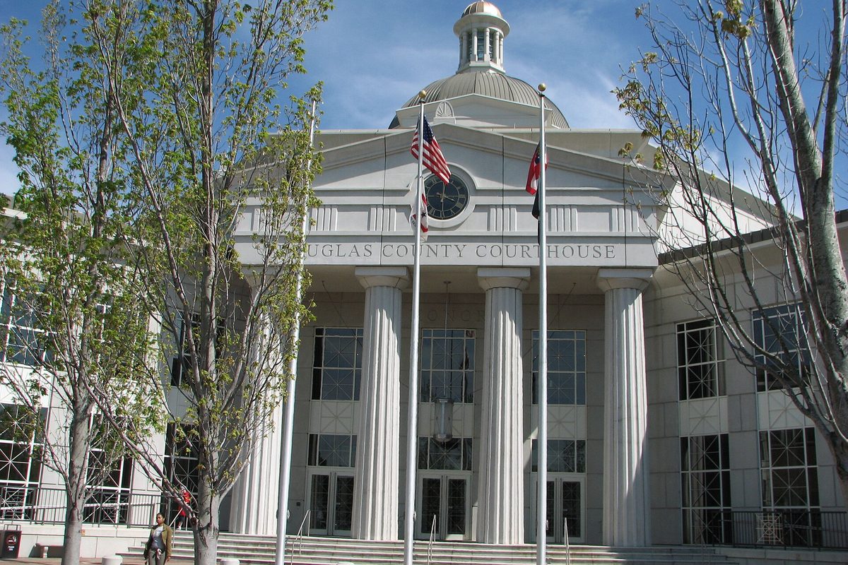 The white Douglas County Courthouse in Douglasville, with tall columns, a clock in the pediment, a domed cupola and two flags out front, beside bare trees