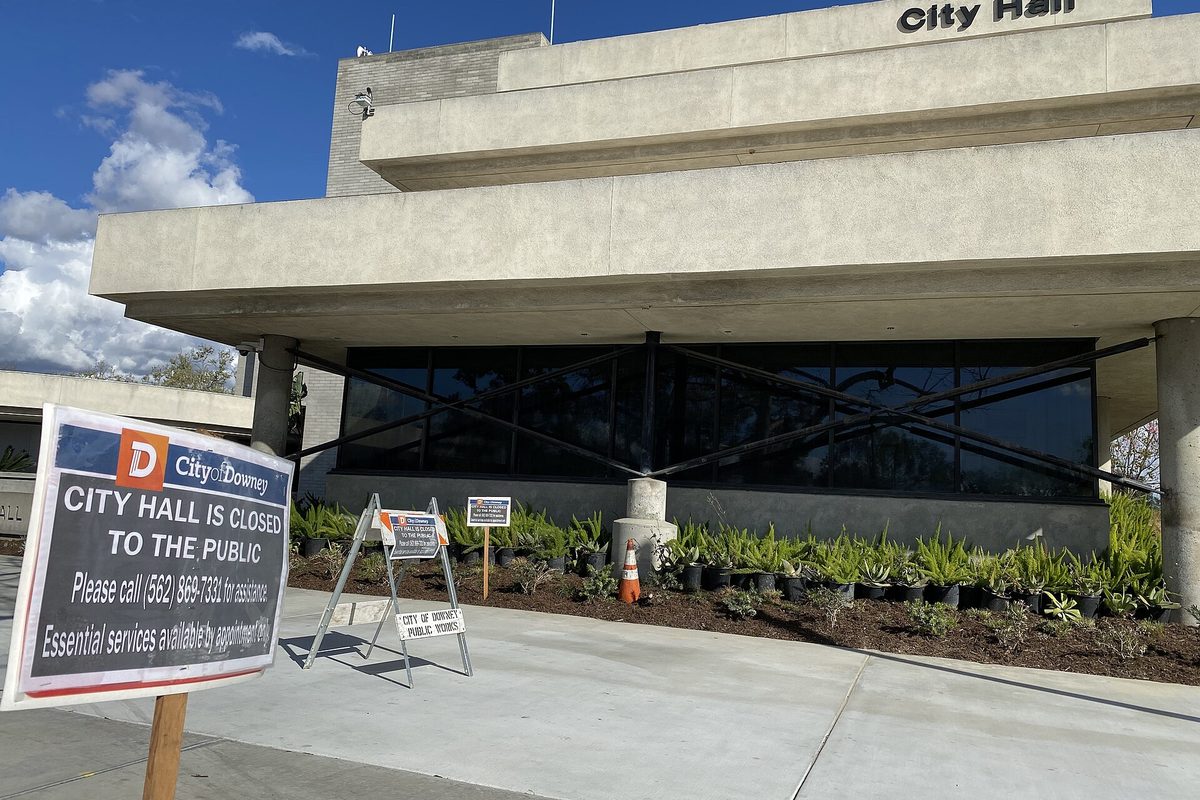 The concrete front of Downey City Hall with a sign reading City Hall is closed to the public, beside a fresh planting bed and a traffic cone