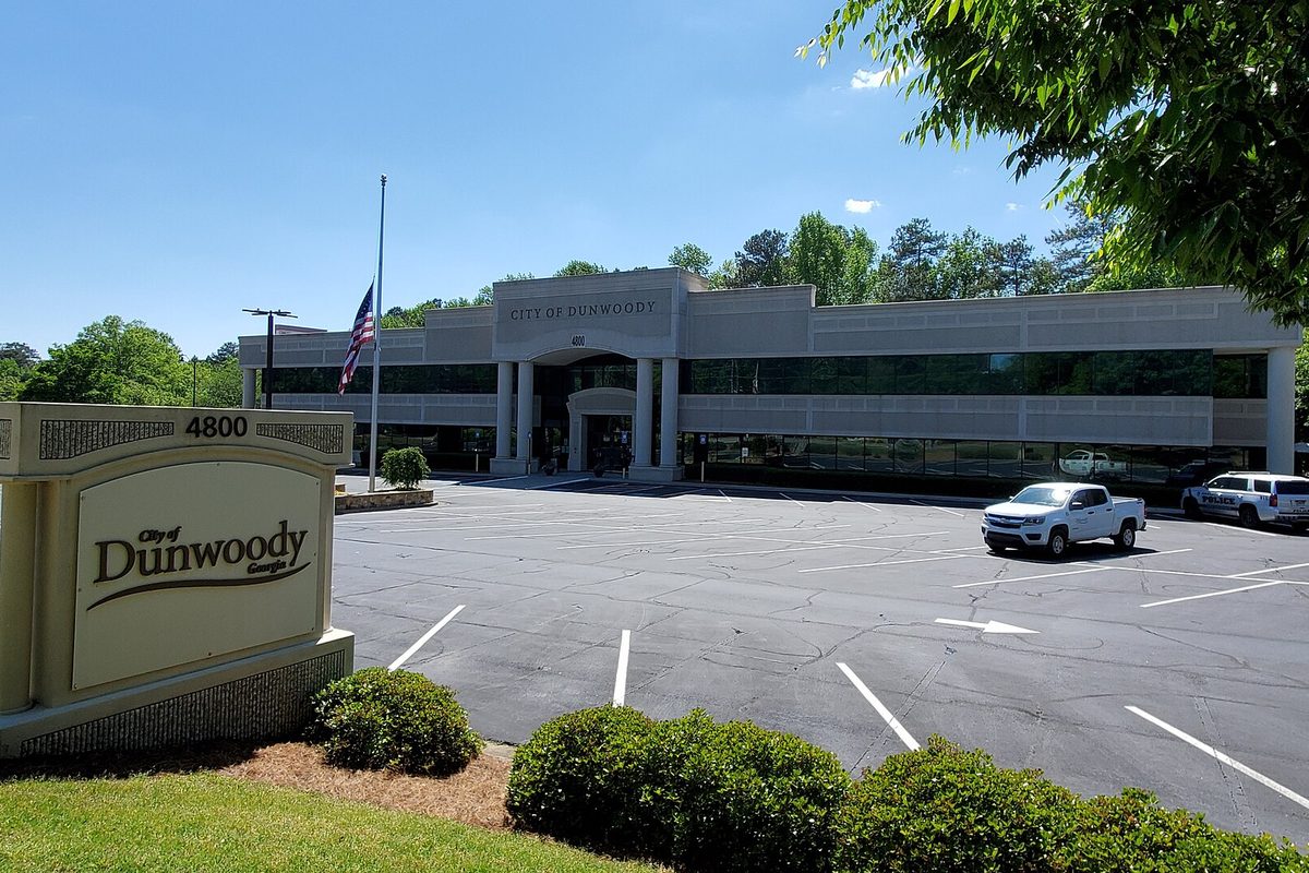 Dunwoody City Hall, a long two-story office building behind a parking lot, with a stone City of Dunwoody address sign in front