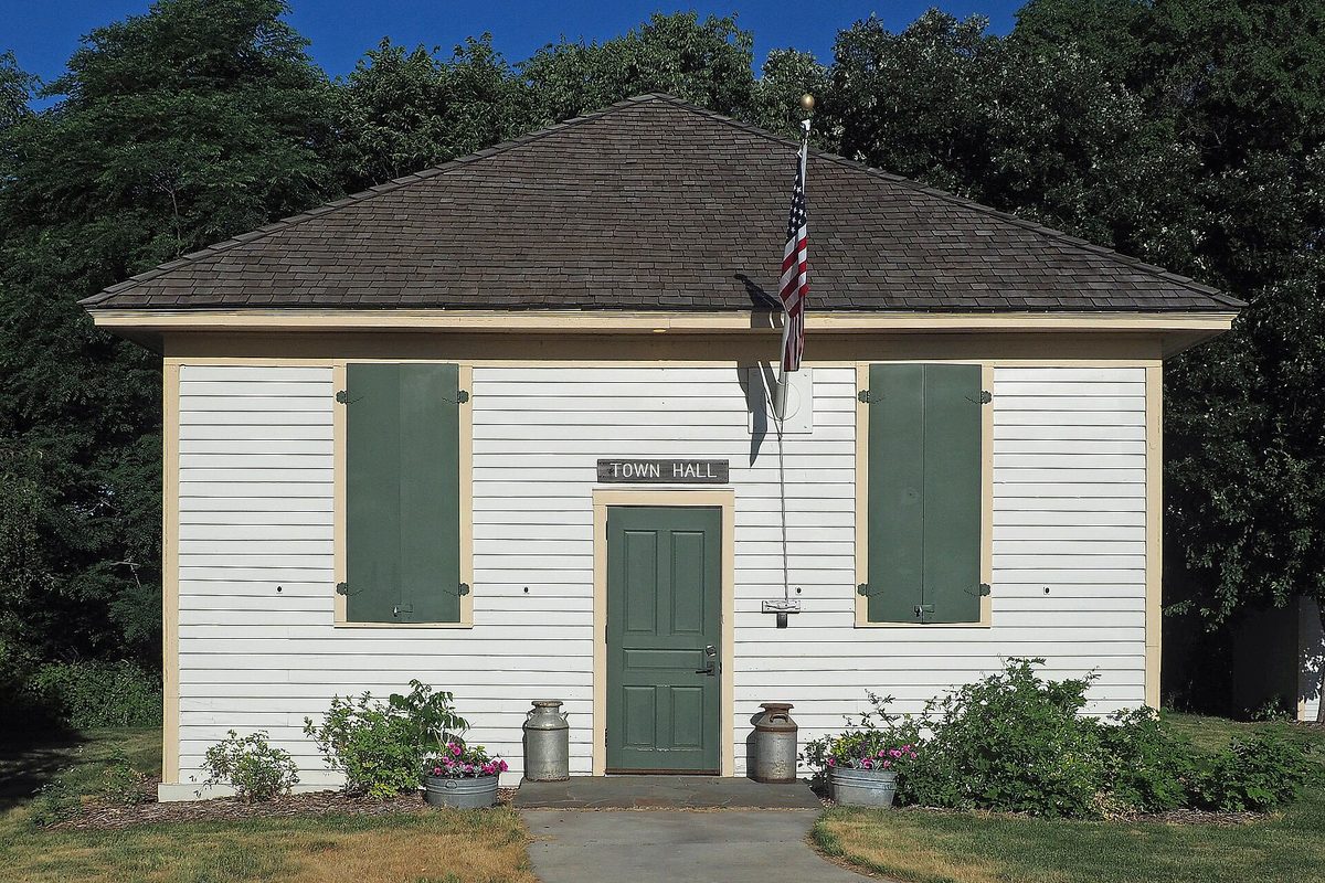 Eagan's small white Historic 1914 Town Hall with green shutters, a green door, milk cans by the steps and an American flag