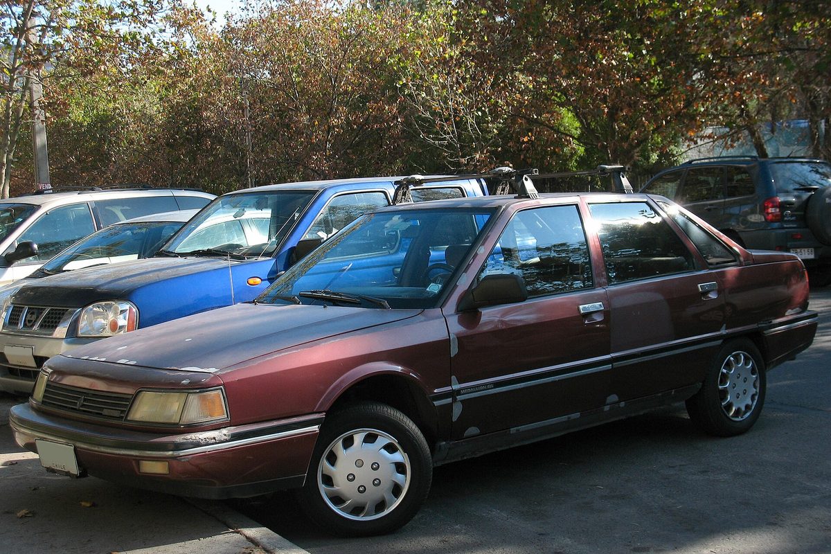A faded maroon Medallion sedan, badged here as a Renault, parked in a lot under autumn trees